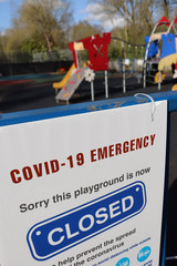 Fototapeta premium A sign that invites people to respect social distances. In the background a closed and empty playground. Covid-19 emergency measures. Coronavirus outbreak. England, United Kingdom. UK