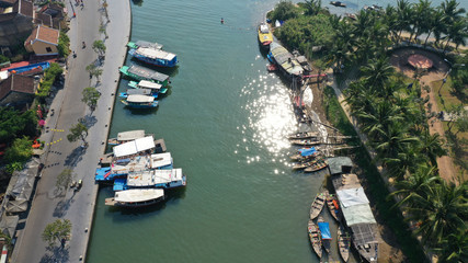 Fototapeta na wymiar Aerial top down view of Hoi An old town on Thu Bon river, Quang Nam province, Vietnam. Unesco world heritage. Boats moored to river embankment. Roof tops. Palm trees