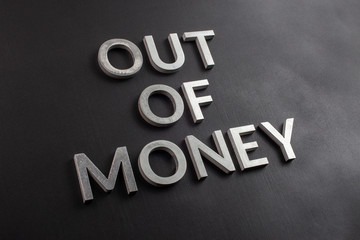 the words out of money laid with white brushed metal letters on flat black surface with diagonal...