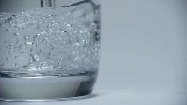 Clear drinking water pours into a clean transparent glass on a white background.