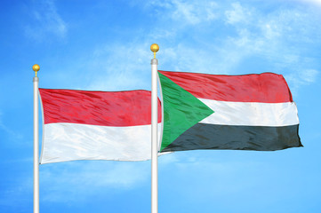 Indonesia and Sudan two flags on flagpoles and blue cloudy sky