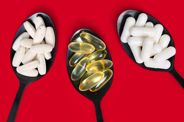 Healthy Supplements on black spoons against red background