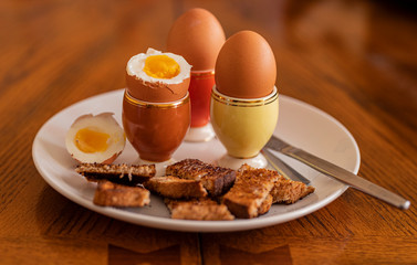 Soft boiled eggs and toast soldiers on a white plate with 60's style egg cups