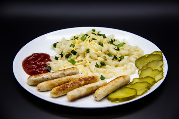Pasta on a plate with cheese on top and green onions. Delicious pasta made from high quality flour with chicken sausage from grill and sliced cucumber from jar. Horns made of flour cooked with cheese