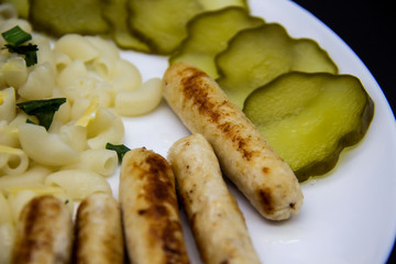 Pasta on a plate with cheese on top and green onions. Delicious pasta made from high quality flour with chicken sausage from grill and sliced cucumber from jar. Horns made of flour cooked with cheese