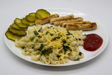 Pasta on a plate with cheese on top and green onions. Delicious pasta made from high quality flour with chicken sausage from grill and sliced cucumber from jar. Horns made of flour cooked with cheese