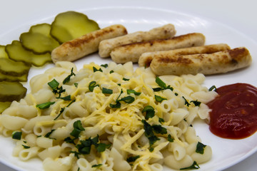 Pasta on a plate with cheese on top and green onions. Delicious pasta made from high quality flour with chicken sausage from grill and sliced cucumber from jar. Horns made of flour cooked with cheese