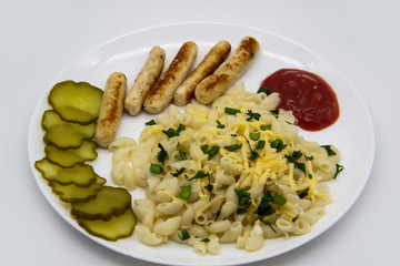 Pasta on a plate with cheese on top and green onions. Delicious pasta made from high quality flour with chicken sausage from grill and sliced cucumber from jar. Horns made of flour cooked with cheese