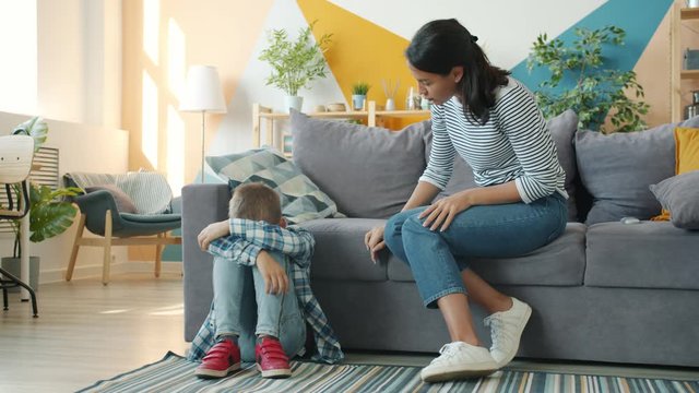 Angry mother is punishing naughty kid talking yelling pushing child who is crying sitting on floor at home. Childhood, discipline and people concept.