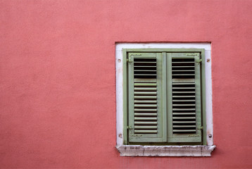 Window with closed shutters on a pink wall