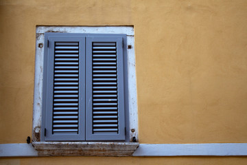 Window with closed shutters on a yellow wall