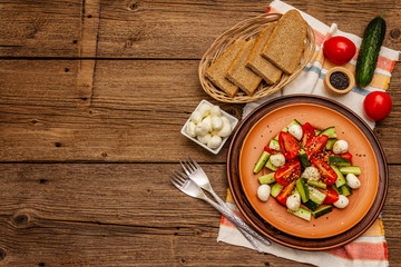Fresh salad from tomato, cucumber and baby mozzarella. Sunny lunch with crusty bread