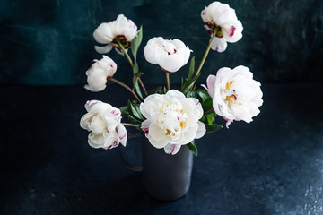 Bouquet of fresh white peonies in a gray vase on a dark background.