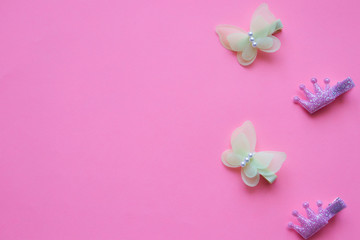 Beautiful baby hair clips in the form of yellow butterflies, with beads and a  crown, lie vertically on a pink background. Place for text, beauty and style with young, children's accessories.