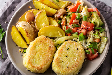 Cooked chops, baked potatoes and vegetable salad, grey plate and napkin. Top view, close up.