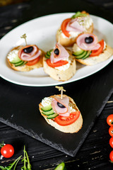 Canapes with cheese, ham, cucumber and tomato on a dark background
