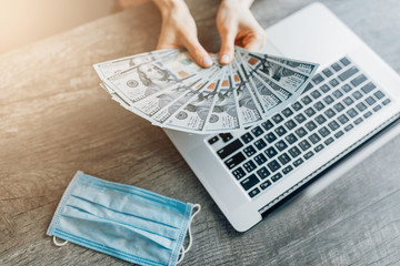 Close-up of hands holding dollar bills against the background of a laptop. Concept of remote work, quarantine, and coronavirus,