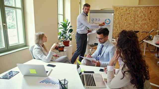 Group of young business people working together in office, coworker conducting a business presentation using flip chart.