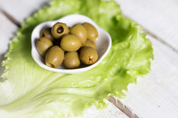 Green olives seedless in white bowl on salad leaf on   wooden background close up