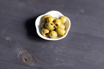 Green olives seedless in white bowl on black wooden background close up