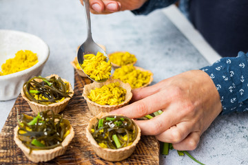 Woman hands make vegan tarts with long rice filling and stuffed with laminaria kelp seaweed salad. Healthy snack. 