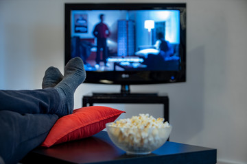 man watching a movie with foot over the table with popcorn 