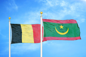 Belgium and Mauritania two flags on flagpoles and blue cloudy sky