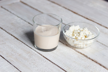 Homemade cottage cheese in bowl and glass of fermented baked milk on white wooden background
