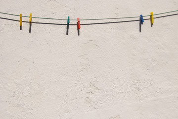 Light gray wall. On the wall hangs a rope with colored clothespins. Background. Free space for text.