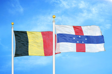 Belgium and Netherlands Antilles two flags on flagpoles and blue cloudy sky