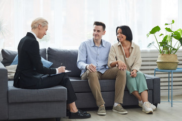 Mature businesswoman sitting on the sofa and concluding the contract with young couple they are going to buy a new house