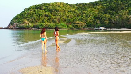 Young women in swimsuits talking on phone, standing on calm shallow lagoon near sandy beach of tropical island in Myanmar