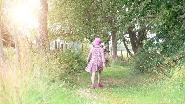 Little girl walking alone on trail in nature. Calm nature scene with sunlight of exploring child. Concept of childhood adventure and lifestyle activity.