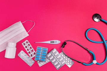 Medical and coronavirus prevention concept flat lay. Medical items and copy space text place on plastic pink background. Mask, thermometer, pills, tablets and stethoscope.