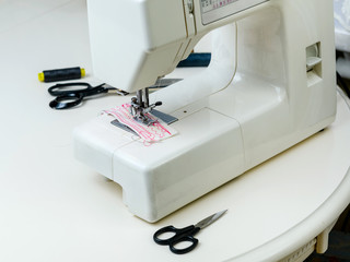 Sewing machine and sewing accessories: scissors, threads, ribbons on the table in the room. Concept - sewing as a hobby