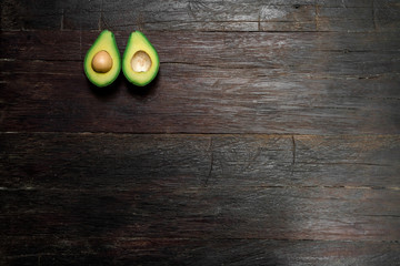 Top view of a ripe avocado halves lying on a wooden background with large area for copy space. One slice with core. Fresh food for a healthy diet.