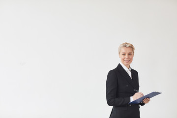 Portrait of successful mature businesswoman in black suit signing a contract and smiling at camera isolated on white background