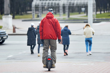 Personal electrical transport, self mobility. Man crosses crosswalk in unicycle. Guy standing on self-balancing personal transporter with single wheel. Electric unicycle.