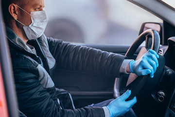 A man driving a car in a protective medical mask and gloves. Safe drive in a taxi during a pandemic coronavirus. Protect the driver and passengers from bacteria and virus infection in quarantine - obrazy, fototapety, plakaty