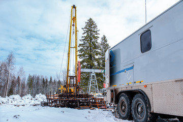 Wireline equipment hanging from top drive ready to be lowered downhole for logging. An oil well engineer works from the back of specialised van to log the condition of steel casing inside an oil well.