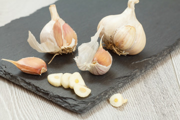 Raw garlic bulbs on a black stone board.