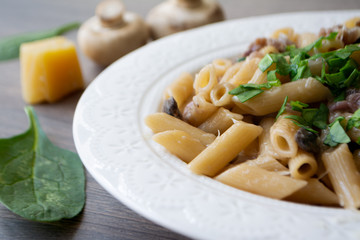 Vegan creamy mushroom garlic pasta with red onions garnished with basil in a white plate with its ingredients in the background, everything on the gray wooden surface