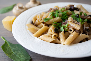 Vegan creamy mushroom garlic pasta with red onions garnished with basil in a white plate with its ingredients in the background, everything on the gray wooden surface
