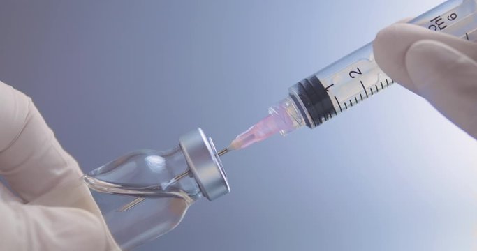 Syringe taking in vaccine from the vial for purpose of immunization or other intravenous therapy. Close-up shot on a grey background.