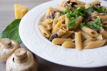 Vegan creamy mushroom garlic pasta with red onions garnished with basil in a white plate with its ingredients in the background, everything on the gray wooden surface
