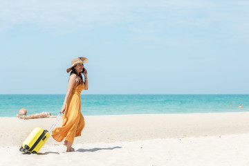 Asian women traveler holding yellow luggage walking and check in smart phone on the beach. Traveler and Tourism planning trips summer vacations with Traveler accessories summertime. Summer Concept
