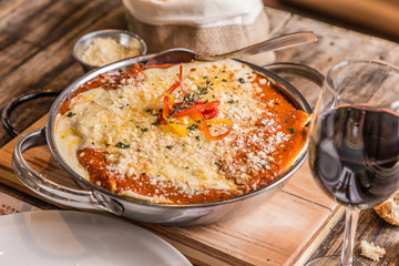 Delicious homemade lasagna with cheese and tomato sauce on a rustic wooden background and red wine