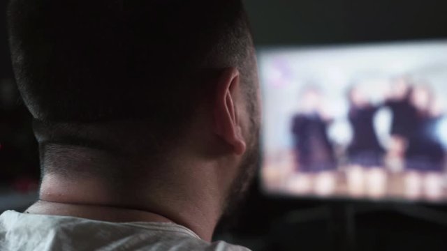 Bearded Caucasian man watching jailbait video on TV screen at home