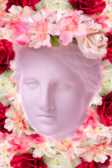 Beautiful young female face and colorful flowers. Plaster antique bust of Venus in a floral wreath. Beauty spring and summer model girl with fresh bouquet.