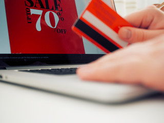 Red credit card in man's hand with computer screen that pictures red sale banner
